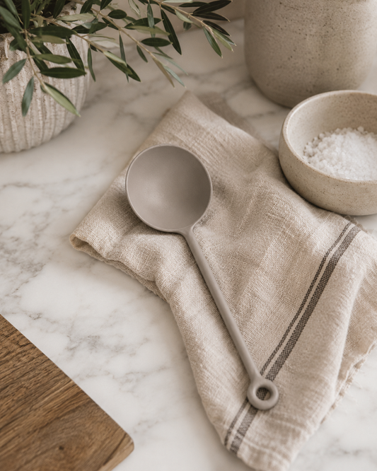 Matte gray stainless steel scoop styled on a marble countertop with a neutral linen towel, ceramic salt bowl, and modern California-inspired kitchen décor.