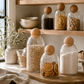 Minimal glass pantry storage jars with cork ball lids styled on a marble countertop in a bright organic modern kitchen