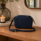 Navy Katie Loxton Isla Crossbody Bag styled on a warm oak console table in a quiet luxury interior with soft neutral decor and editorial lighting.