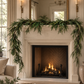 Norfolk pine garland draped across a stone fireplace mantel in a warm neutral Christmas living room.