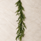 60-inch Norfolk pine garland with long feathery green branches displayed on a neutral marble backdrop.