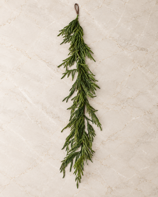 60-inch Norfolk pine garland with long feathery green branches displayed on a neutral marble backdrop.