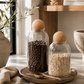 Luxury organic modern pantry shelf styling featuring clear glass storage jars with oversized cork ball lids and neutral kitchen decor