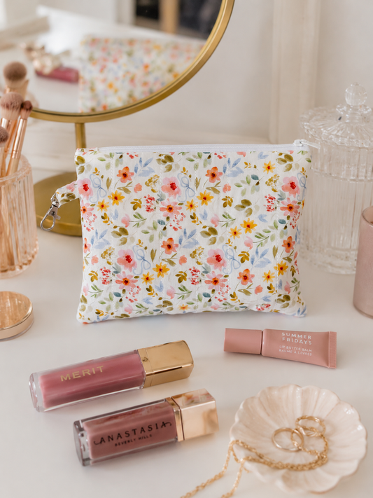 Petal & Posies medium quilted zipper pouch styled on a makeup vanity with beauty essentials, jewelry, and a gold mirror.