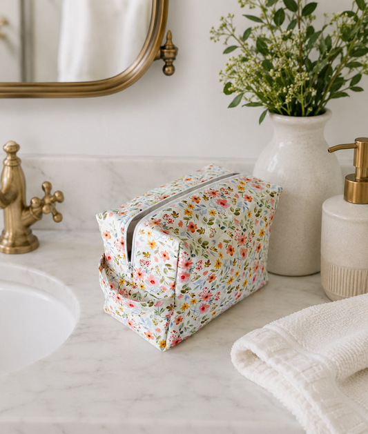 Petal & Posies quilted cosmetic bag styled on a modern bathroom vanity with brass fixtures, a ceramic vase, greenery, and marble countertop.
