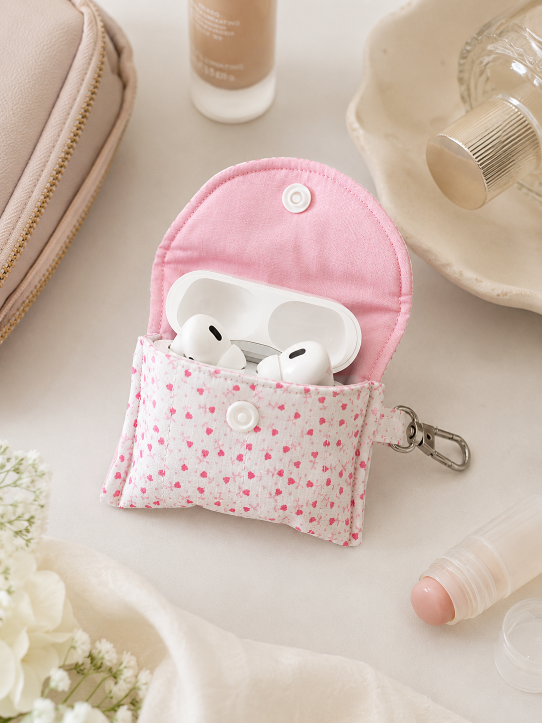 Pink floral quilted AirPods case styled with beauty products and feminine accessories in soft neutral lighting