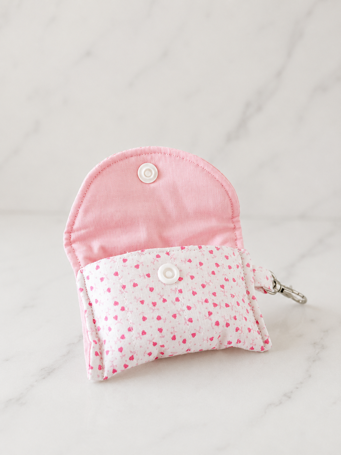 Pink floral quilted AirPods case with snap closure on neutral marble studio background