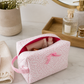 Pink floral makeup bag styled with beauty essentials on luxury bathroom countertop in soft natural light