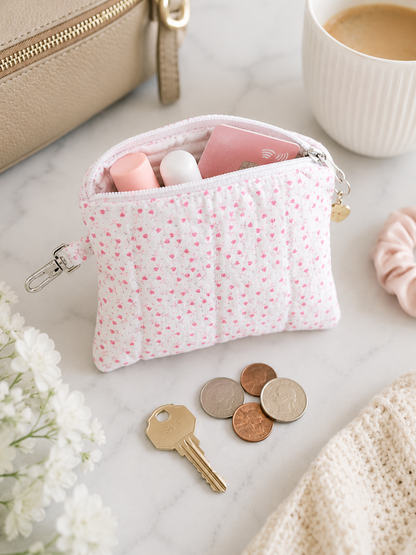 Pink floral quilted coin purse styled with cash, cards, keys, and feminine accessories on white marble countertop