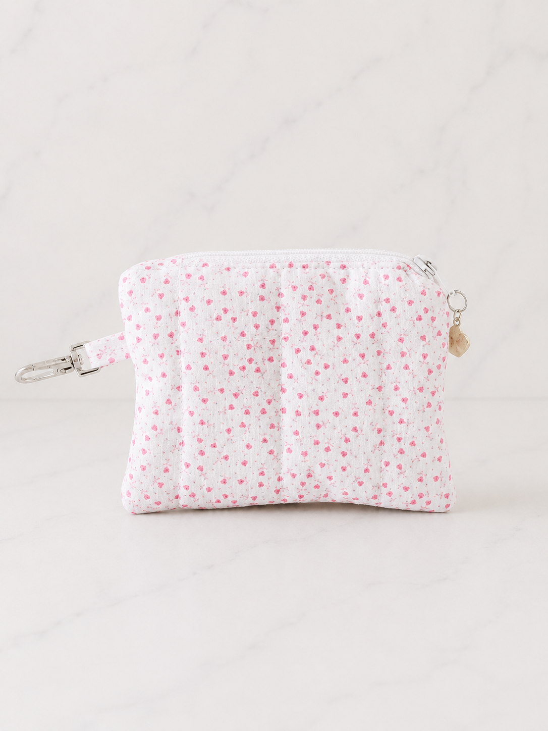 Pink floral quilted coin purse with silver zipper and heart charm on white marble background in soft studio lighting