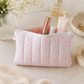 Pink floral quilted cosmetic pouch styled with beauty products and neutral feminine decor in soft natural lighting