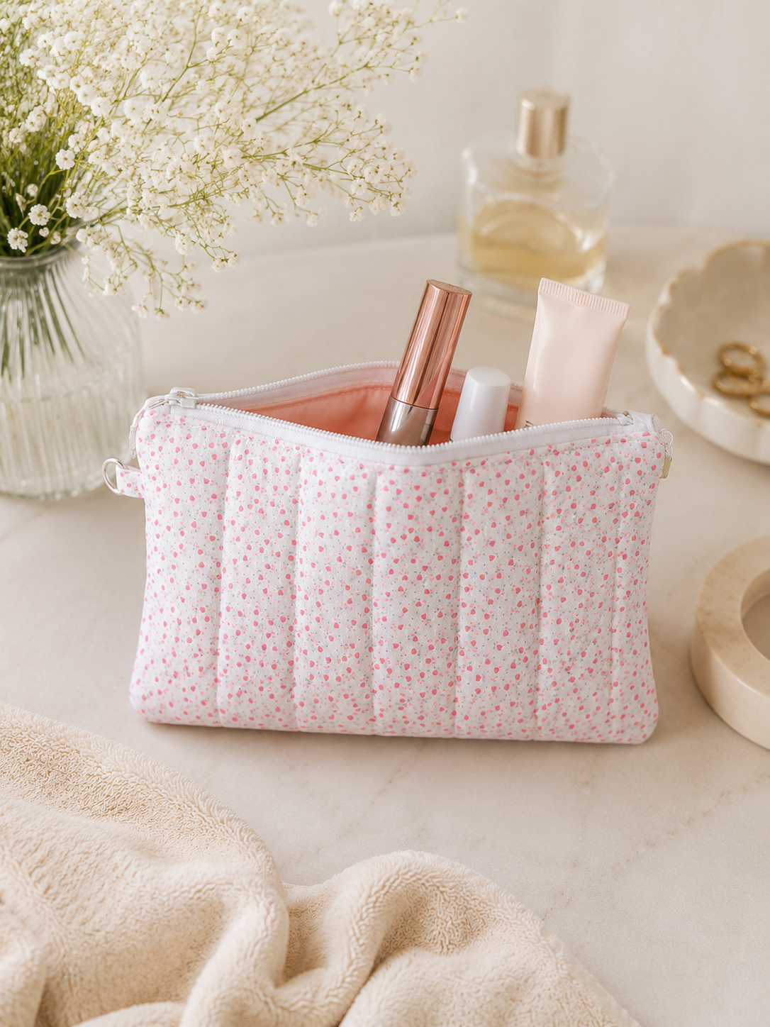Pink floral quilted cosmetic pouch styled with beauty products and neutral feminine decor in soft natural lighting