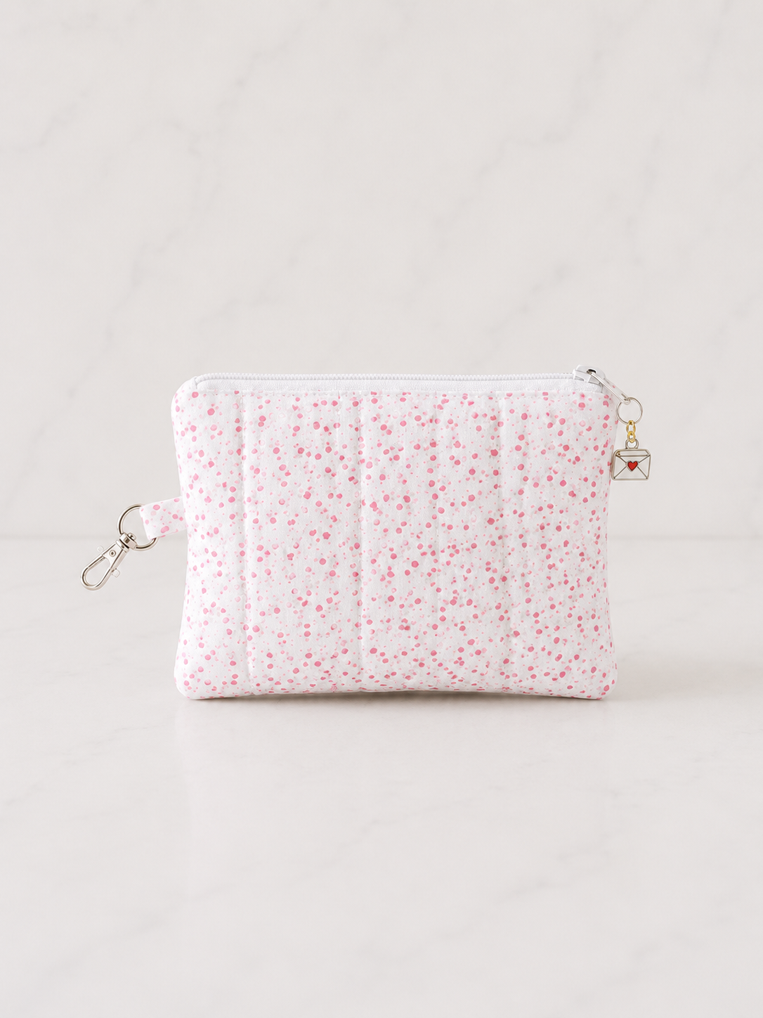 Pink floral quilted medium zipper pouch on luxury white marble background in clean editorial studio lighting