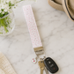 Pink floral wristlet keychain styled with car keys, neutral handbag, and soft feminine accessories on marble surface