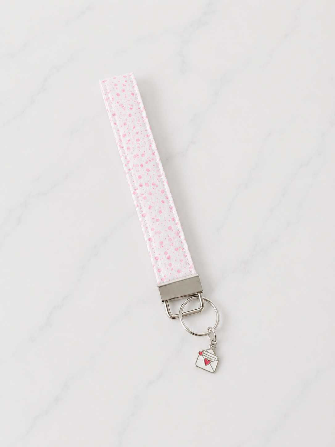 Pink floral fabric wristlet keychain with silver hardware and envelope charm on white marble studio background