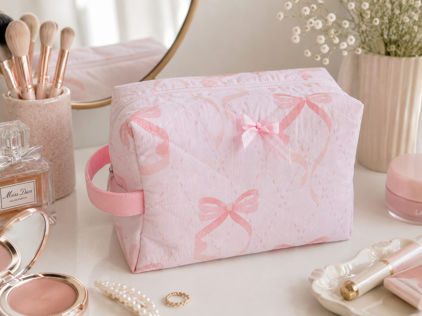 Pink Ribbon quilted makeup bag featuring a soft pink bow print with coordinating gingham bow detail, styled on a bright vanity with everyday beauty essentials.