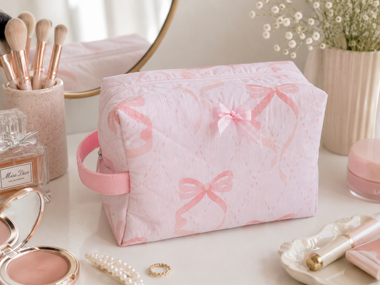 Pink Ribbon quilted makeup bag featuring a soft pink bow print with coordinating gingham bow detail, styled on a bright vanity with everyday beauty essentials.