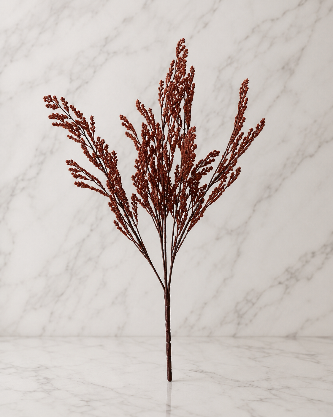Rust brown faux astilbe stem displayed against a white marble studio backdrop, highlighting its natural texture and rich earthy color.