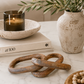 Weathered wood chain link decor styled on a marble coffee table with neutral books, candle, olive branches, and warm organic decor.