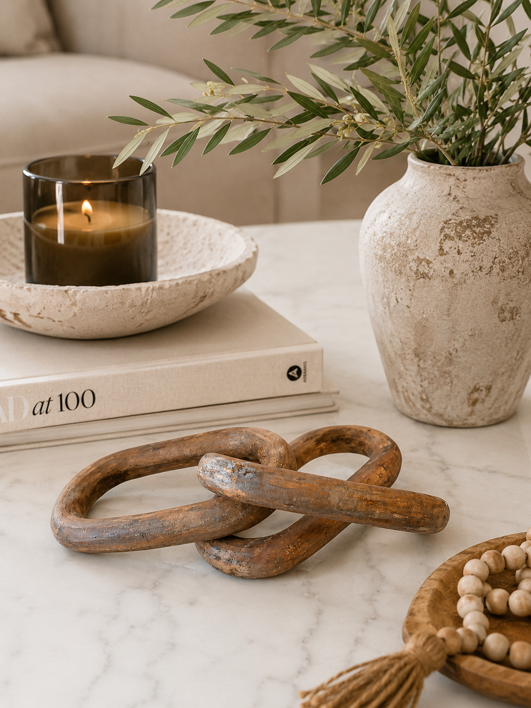 Weathered wood chain link decor styled on a marble coffee table with neutral books, candle, olive branches, and warm organic decor.