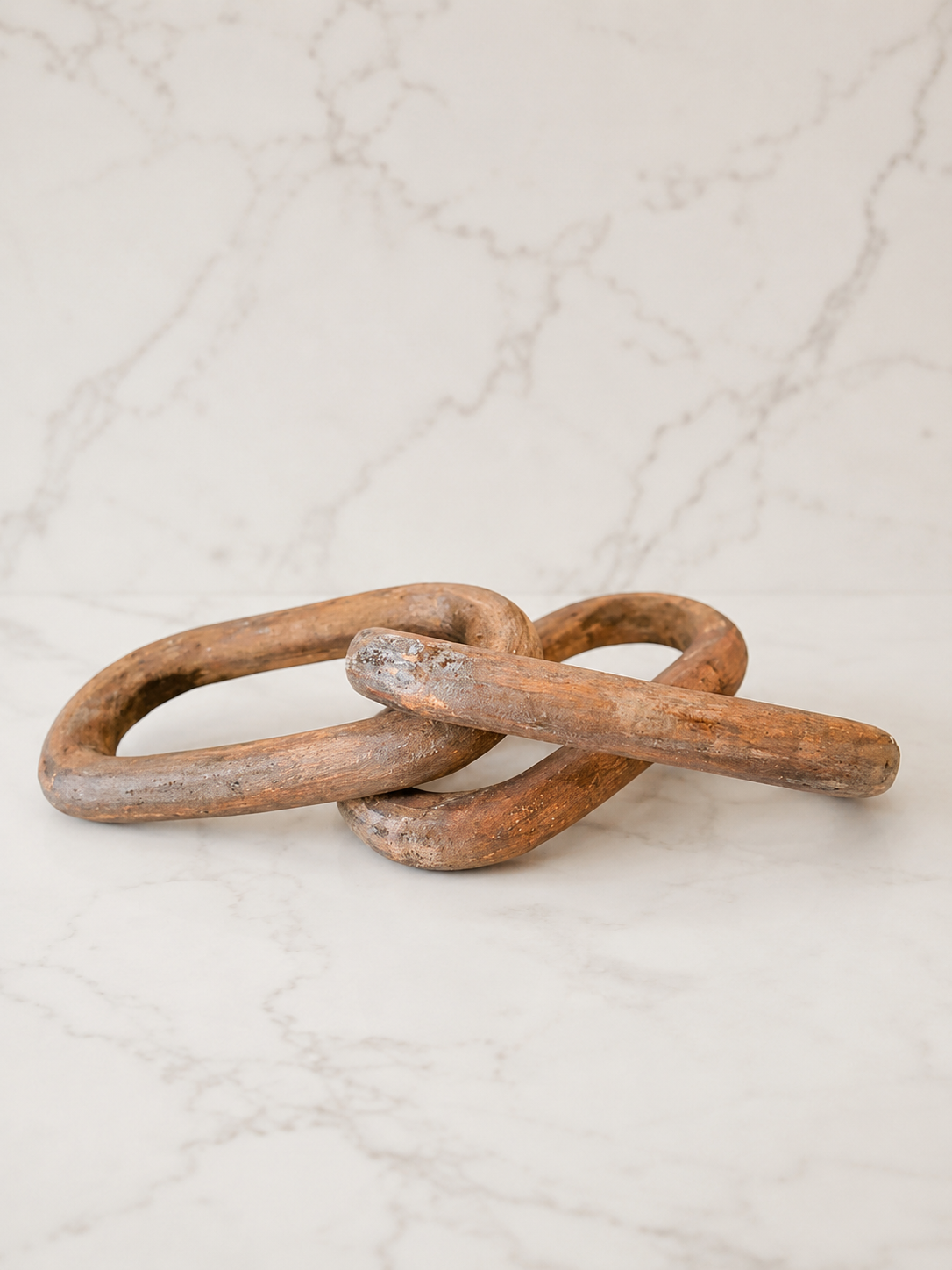 Rustic carved wood chain link decor styled on creamy ivory marble with a minimal luxury studio backdrop.