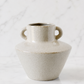 Speckled ivory ceramic vase with dual loop handles on white marble background in soft luxury studio lighting