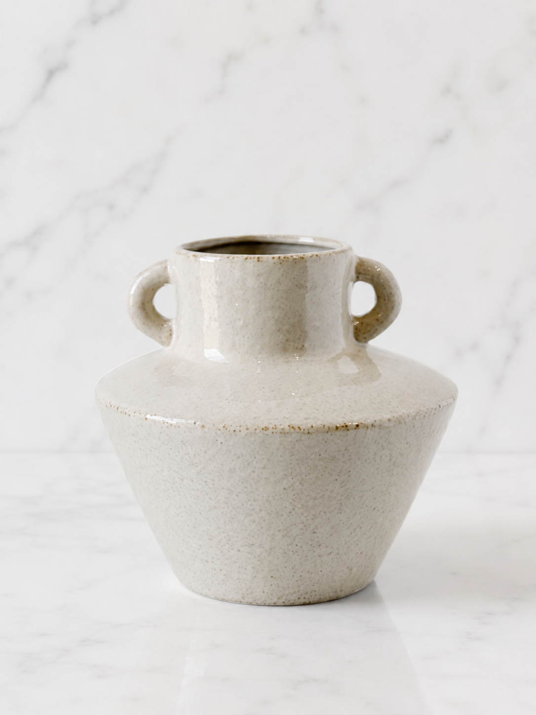 Speckled ivory ceramic vase with dual loop handles on white marble background in soft luxury studio lighting