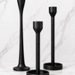 Set of three black cast iron taper candle holders in varying heights styled on a white marble surface with a soft neutral studio backdrop