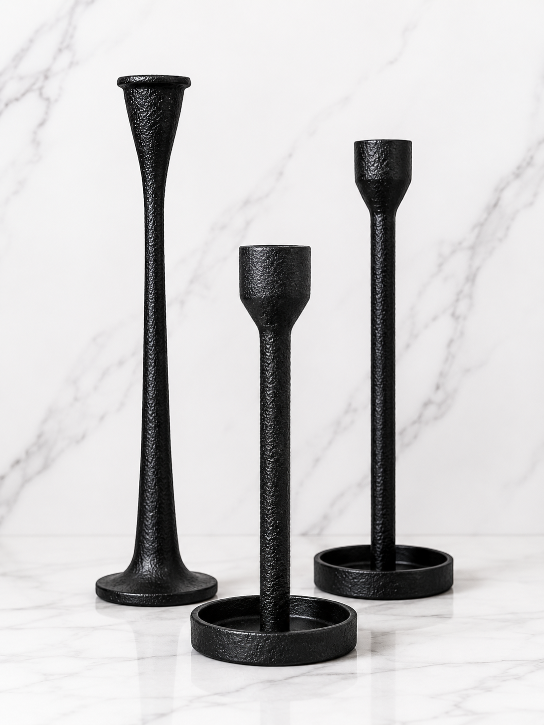 Set of three black cast iron taper candle holders in varying heights styled on a white marble surface with a soft neutral studio backdrop