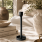 Black cast iron taper candle holder styled on a neutral coffee table with stacked design books, textured ceramics, olive branches, and soft natural light in a warm modern living space.