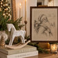 Framed vintage Santa Claus sketch displayed on a wooden console with a white rocking horse, taper candles, and timeless Christmas decorations.