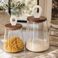 Luxury glass pantry canisters with walnut wood lids and white marble handles styled with pasta and rice on marble countertop in California coastal kitchen