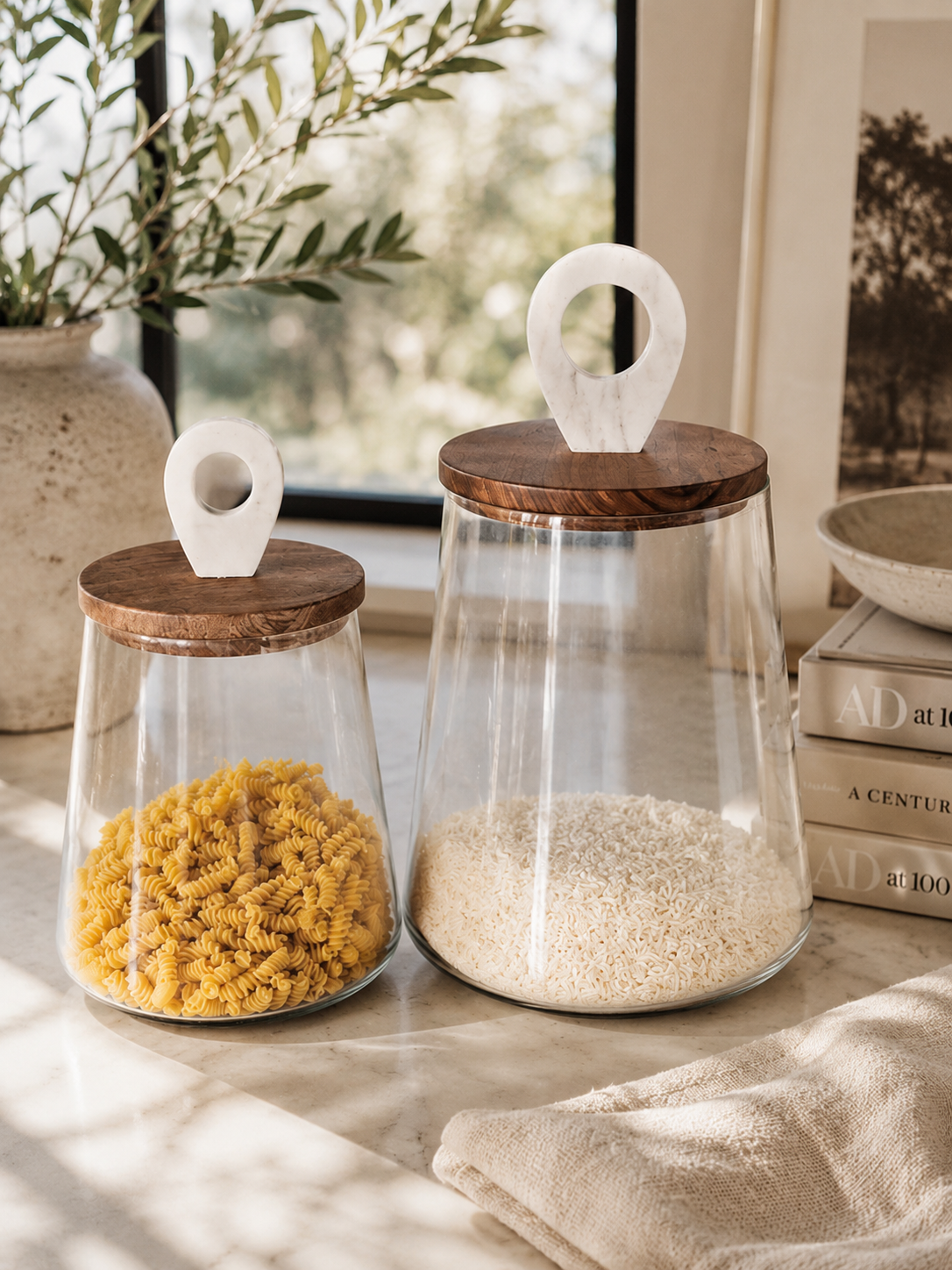 Luxury glass pantry canisters with walnut wood lids and white marble handles styled with pasta and rice on marble countertop in California coastal kitchen