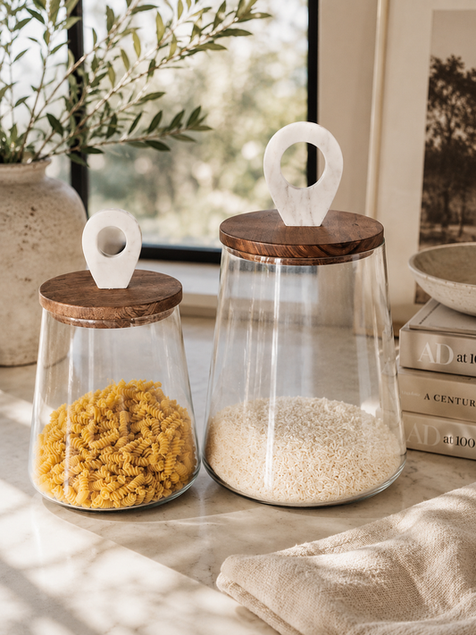 Luxury glass pantry canisters with walnut wood lids and white marble handles styled with pasta and rice on marble countertop in California coastal kitchen