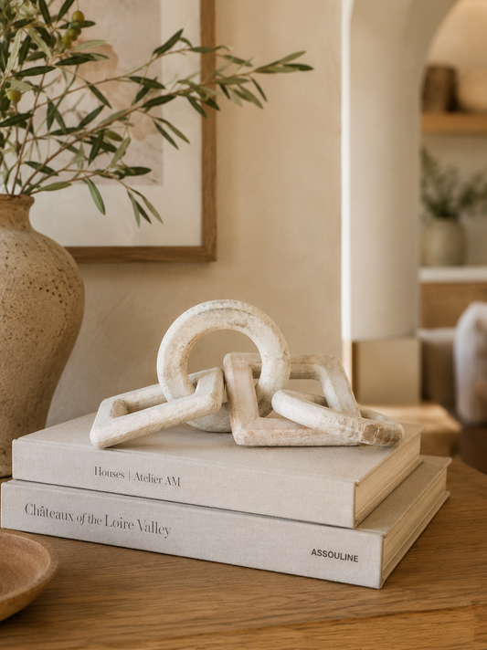 Whitewashed mango wood decorative chain styled on stacked coffee table books with a ceramic vase and olive branches in a modern California-inspired living room.