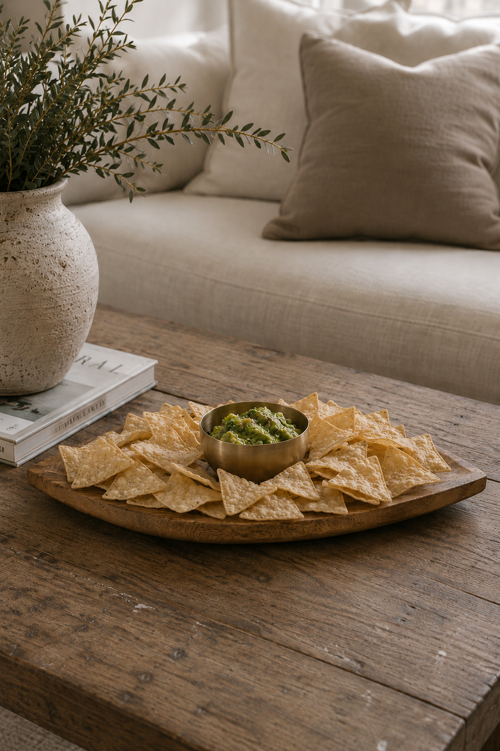 Wood chip and dip serving platter with brass bowl styled on a coffee table with tortilla chips, guacamole, and cocktails in a modern California-inspired living room.