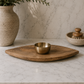 Wood serving platter with a removable brass dip bowl displayed on a white marble countertop against a marble backdrop in a minimalist studio setting.