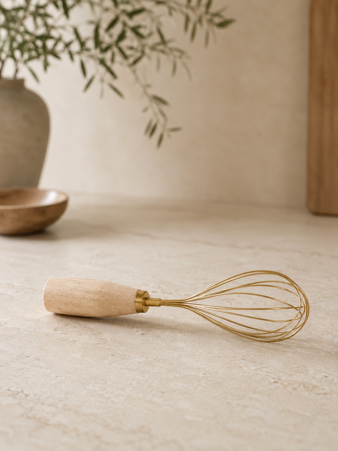 Wooden-handled whisk on a neutral surface with a plant in the background