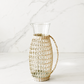 Handwoven rattan wrapped glass pitcher styled in a minimal marble studio setting with soft shadows and airy neutral tones.