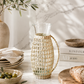 Clear glass pitcher with handcrafted woven rattan sleeve photographed on a soft marble backdrop with clean studio styling and natural light.